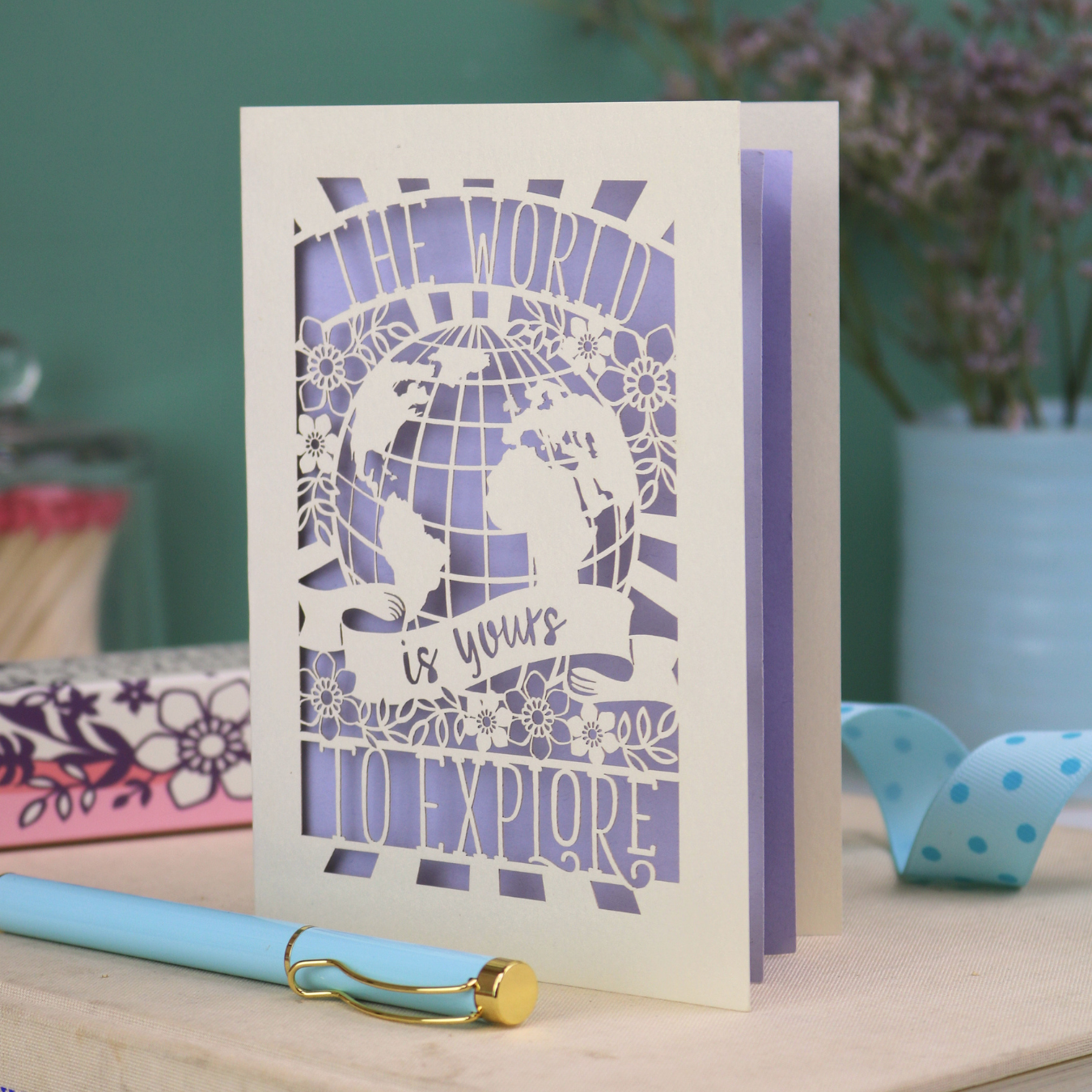 Greeting card with laser cut design and 'The world is yours to explore' text on a wooden surface.