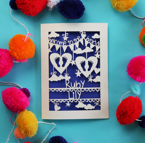 A personalised papercut twins card that says "Welcome to the World" at the top, has two pairs of baby feet in hearts in the middle and the babies' names underneath.  - 