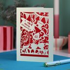 A laser cut 'Merry Un-Birthday' card with pen and stationery items on a blue surface.