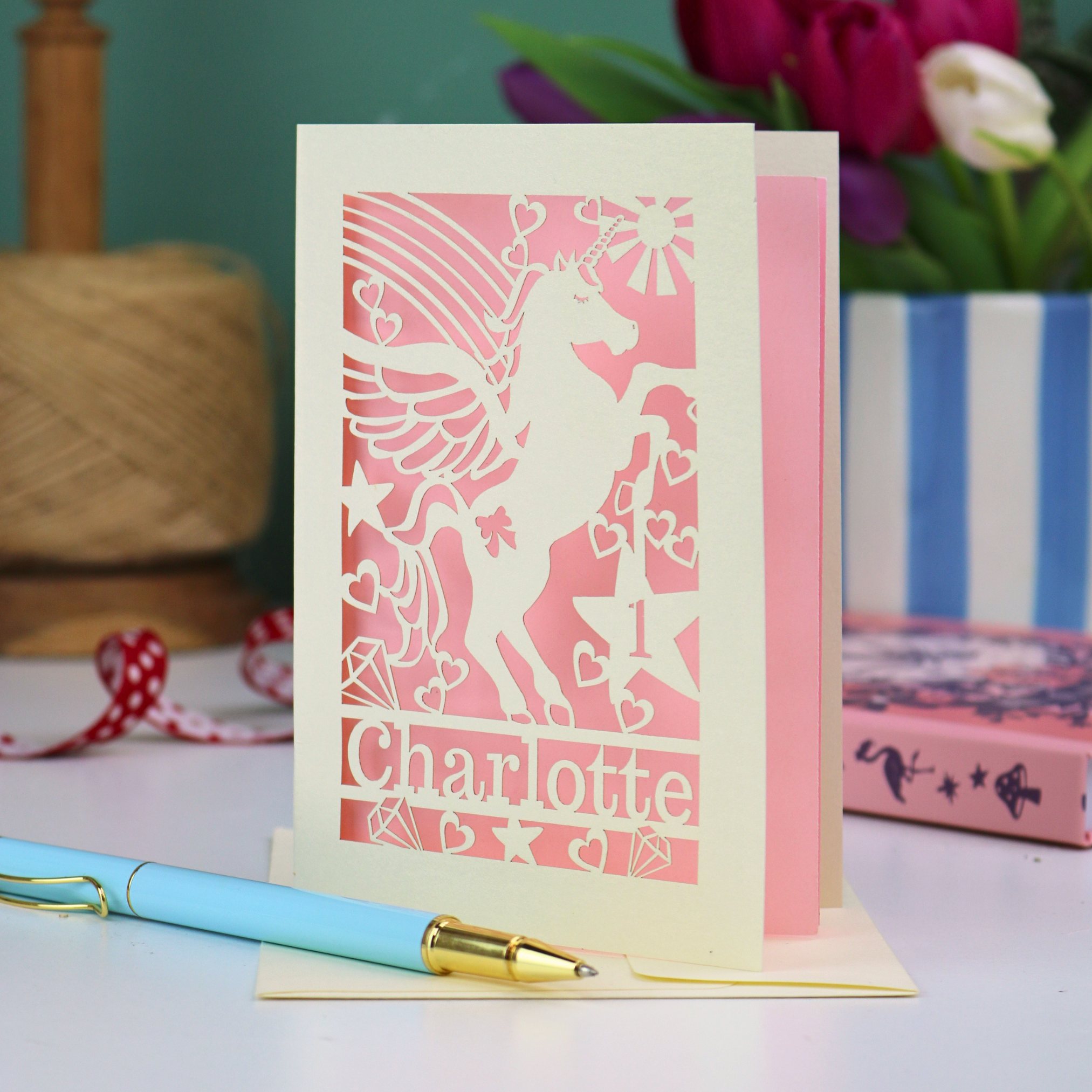 A personalised 1st birthday card for girls, with cut out unicorn design, the age "1" cut out from inside a star shape, and personalised with the name "Charlotte"
