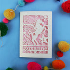 Paper cut out 1st birthday card with a unicorn with 'Roxanne' on a blue background with colourful pom-poms.
