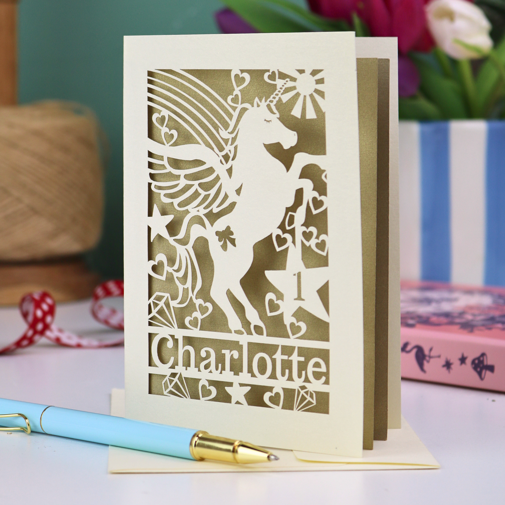 A laser cut keepsake 1st birthday card with cut out unicorn design, the age "1" cut out from inside a star shape, and personalised with the name "Charlotte"