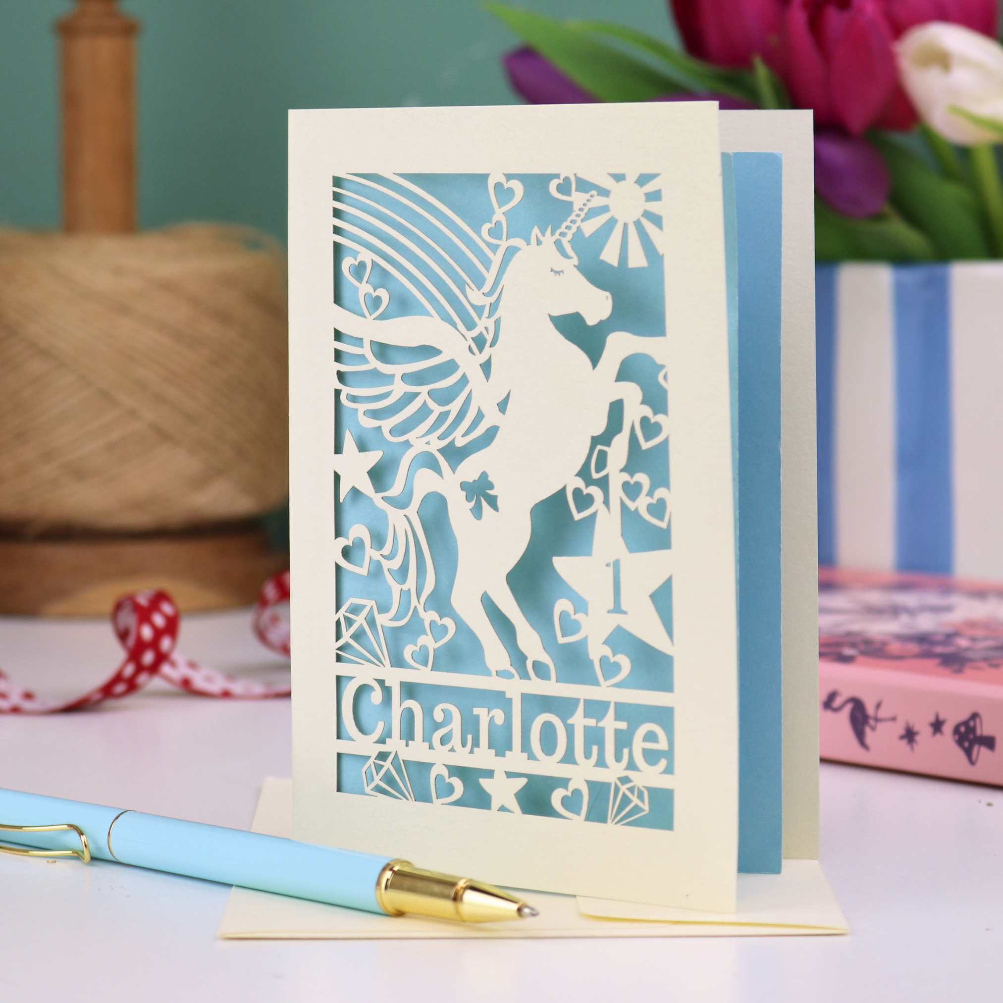 A laser cut 1st birthday card for granddaughters, with cut out unicorn design, the age "1" cut out from inside a star shape, and personalised with the name "Charlotte"
