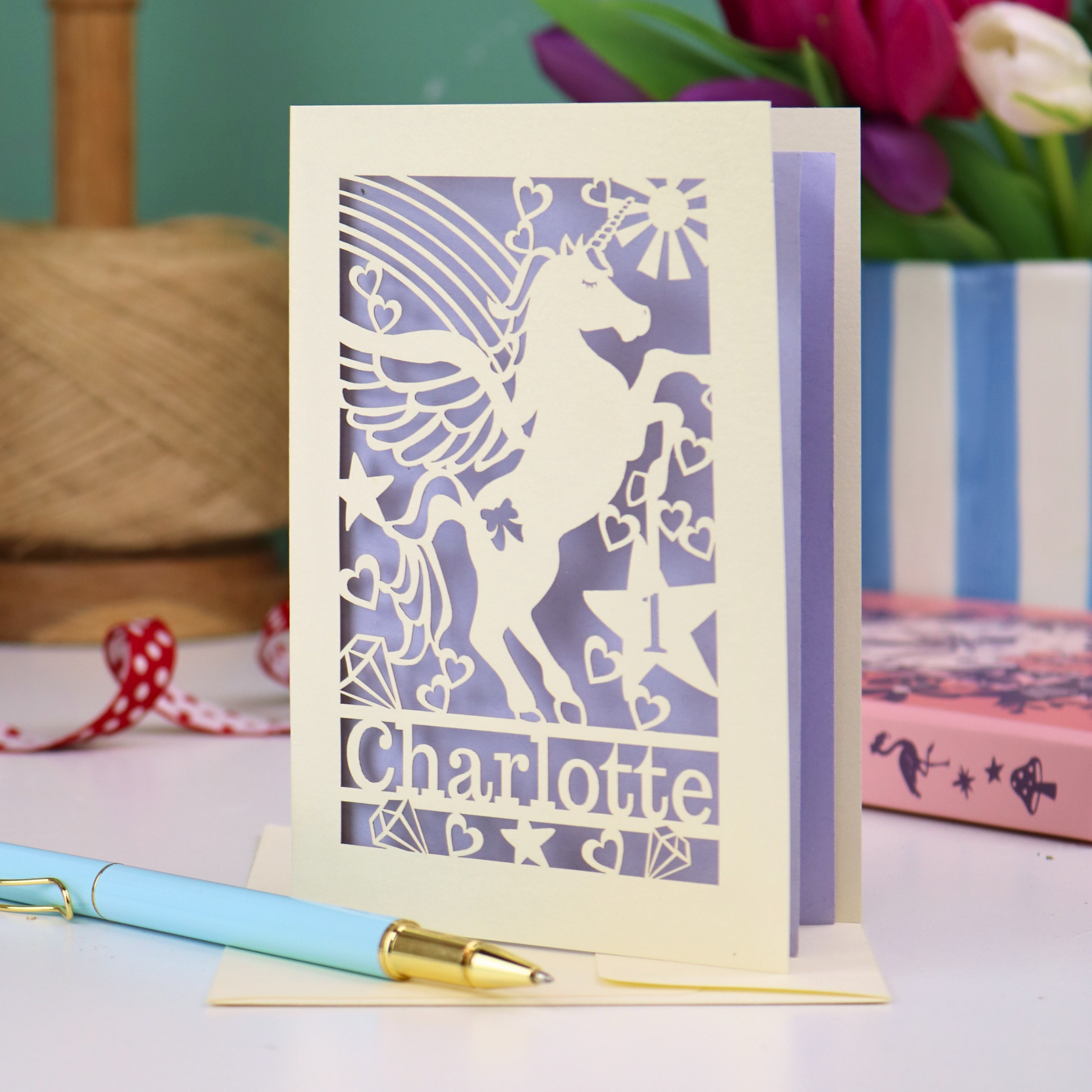 A laser cut personalised 1st birthday card with cut out unicorn design, the age "1" cut out from inside a star shape, and personalised with the name "Charlotte"