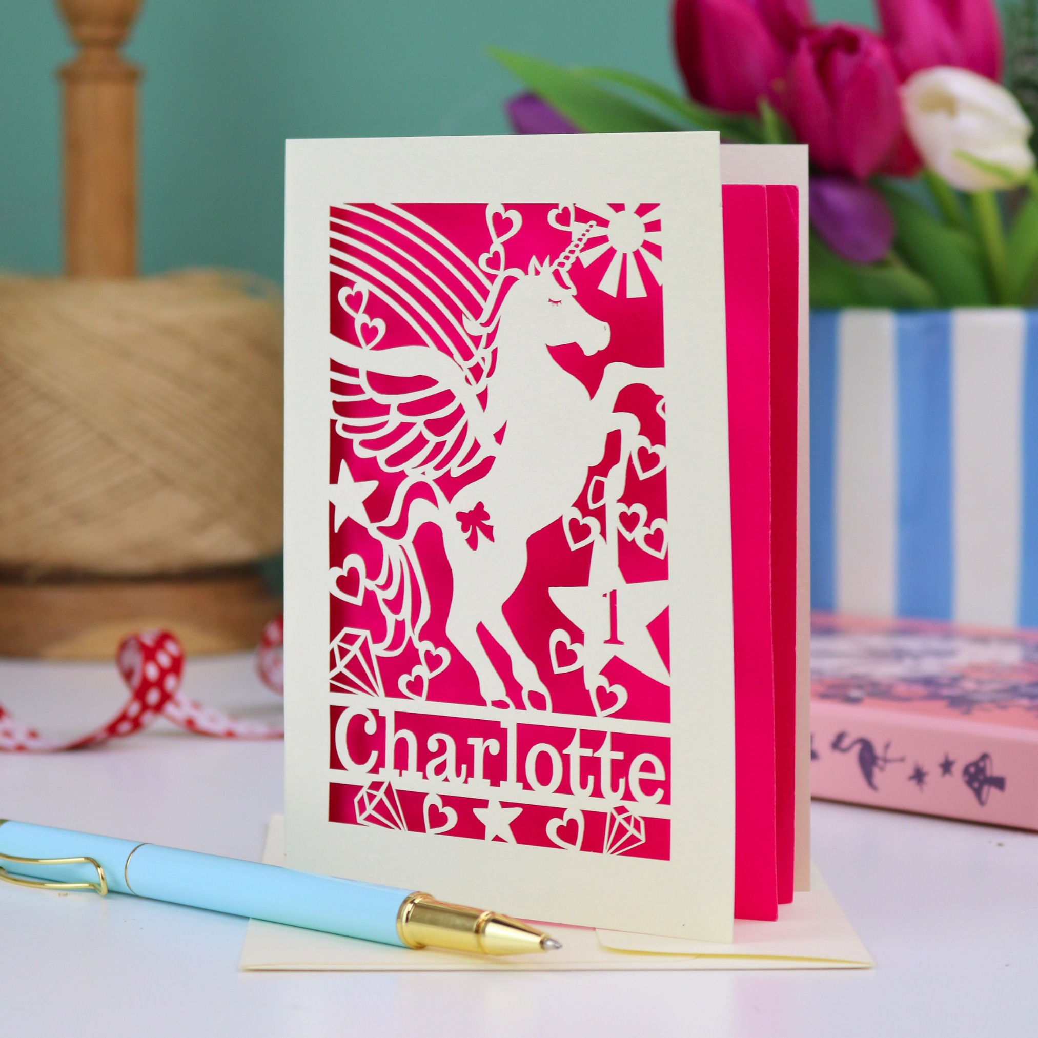 A laser cut 1st birthday card with cut out unicorn design, the age "1" cut out from inside a star shape, and personalised with the name "Charlotte"