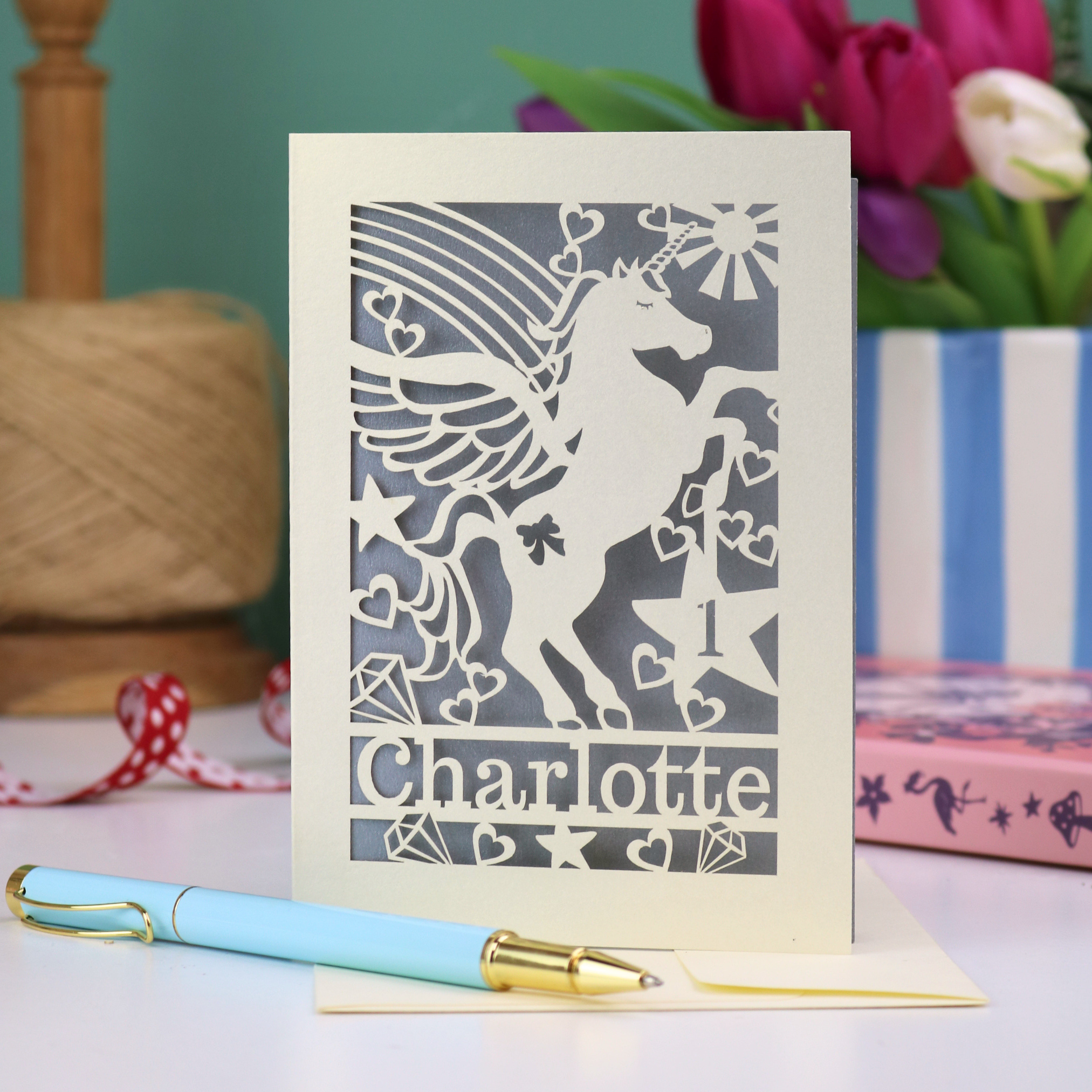 A laser cut 1st birthday card for daughters, with cut out unicorn design, the age "1" cut out from inside a star shape, and personalised with the name "Charlotte"