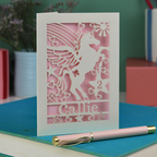 Laser cut Birthday Card with unicorn design and 'Callie' text on a blue surface with a pen.