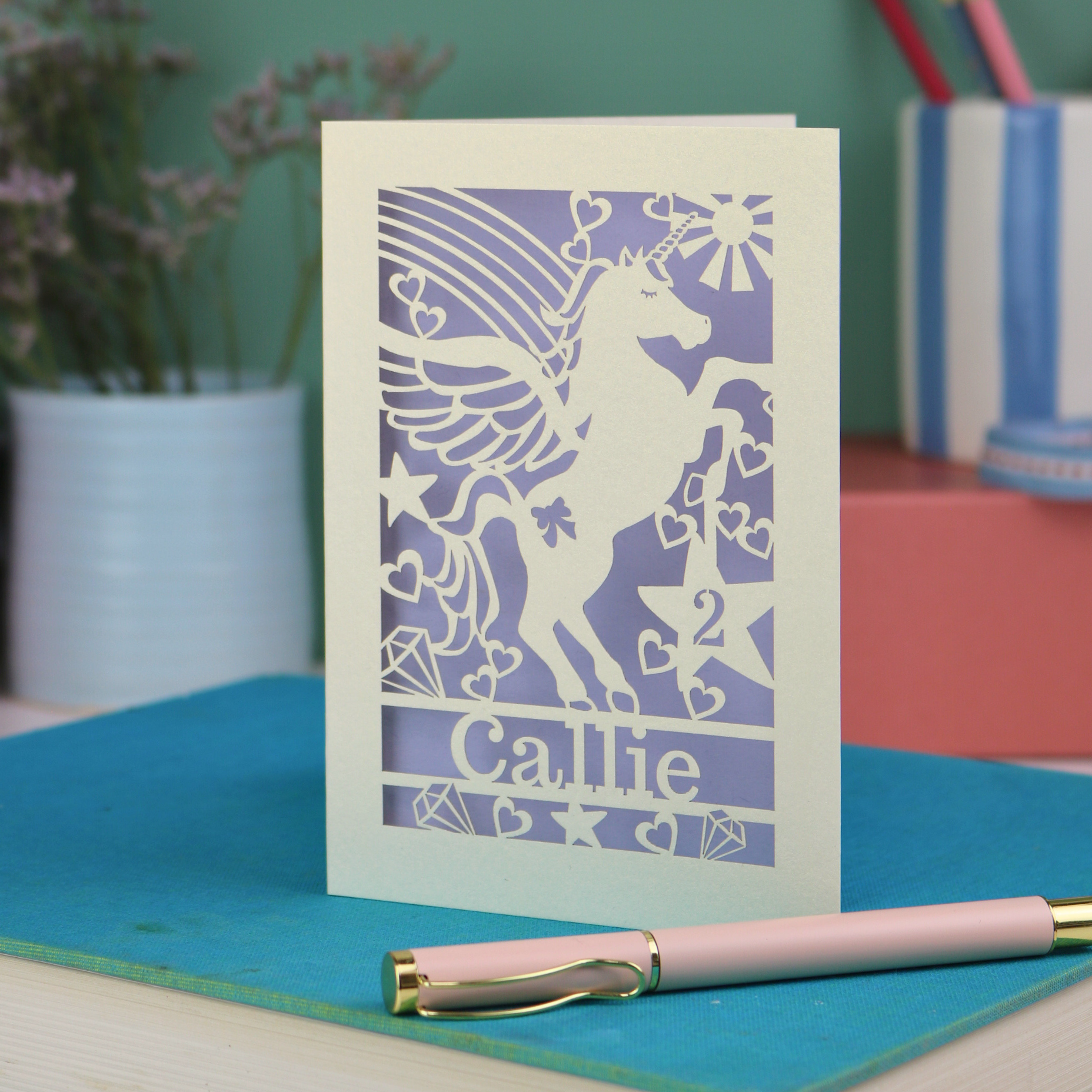 Laser cut Birthday Card with unicorn design and 'Callie' text on a blue surface with a pen.