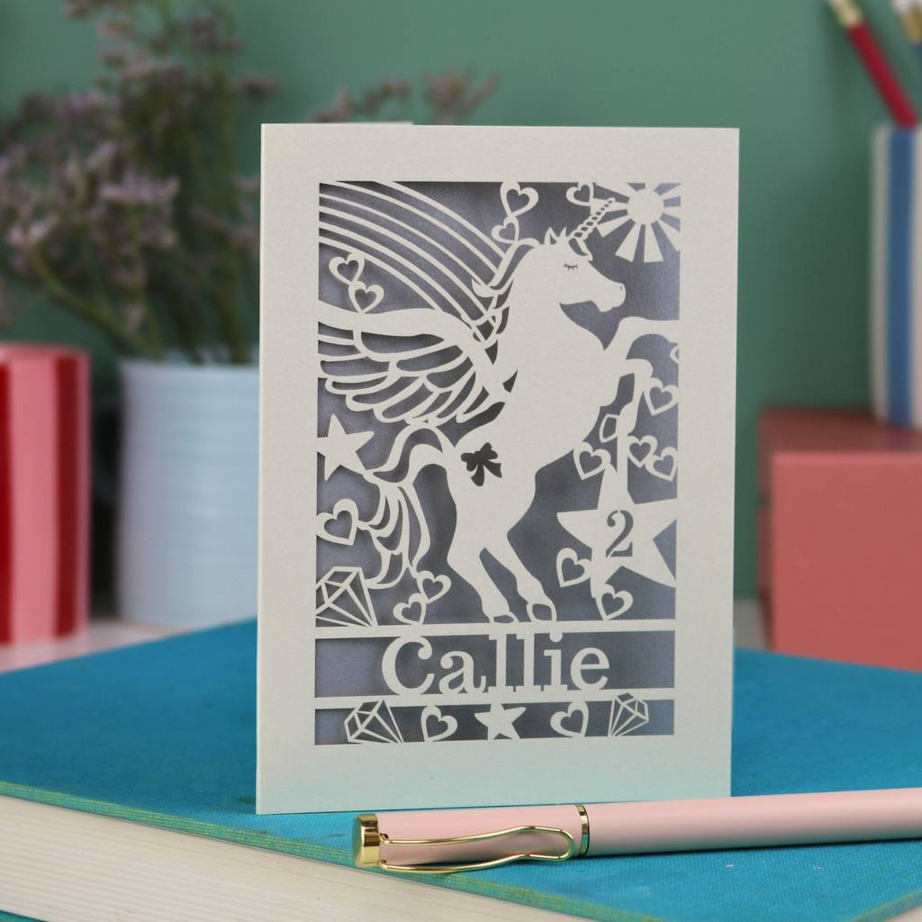 Laser cut Birthday Card with unicorn design and 'Callie' text on a blue surface with a pen.