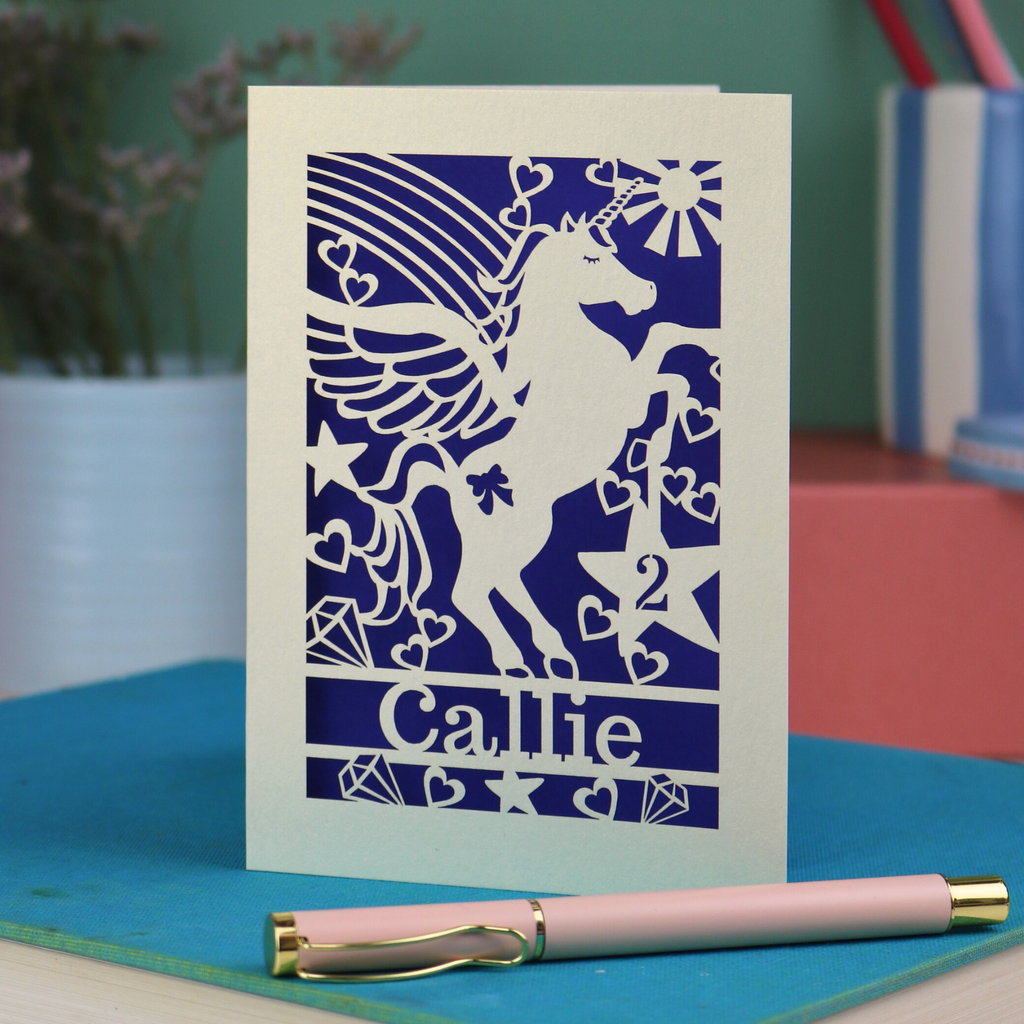 Laser cut Birthday Card with unicorn design and 'Callie' text on a blue surface with a pen.