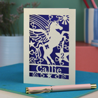 Laser cut Birthday Card with unicorn design and 'Callie' text on a blue surface with a pen.