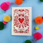 Personalised Valentine's Day card with decorative heart design on a blue background with colourful pom-poms.