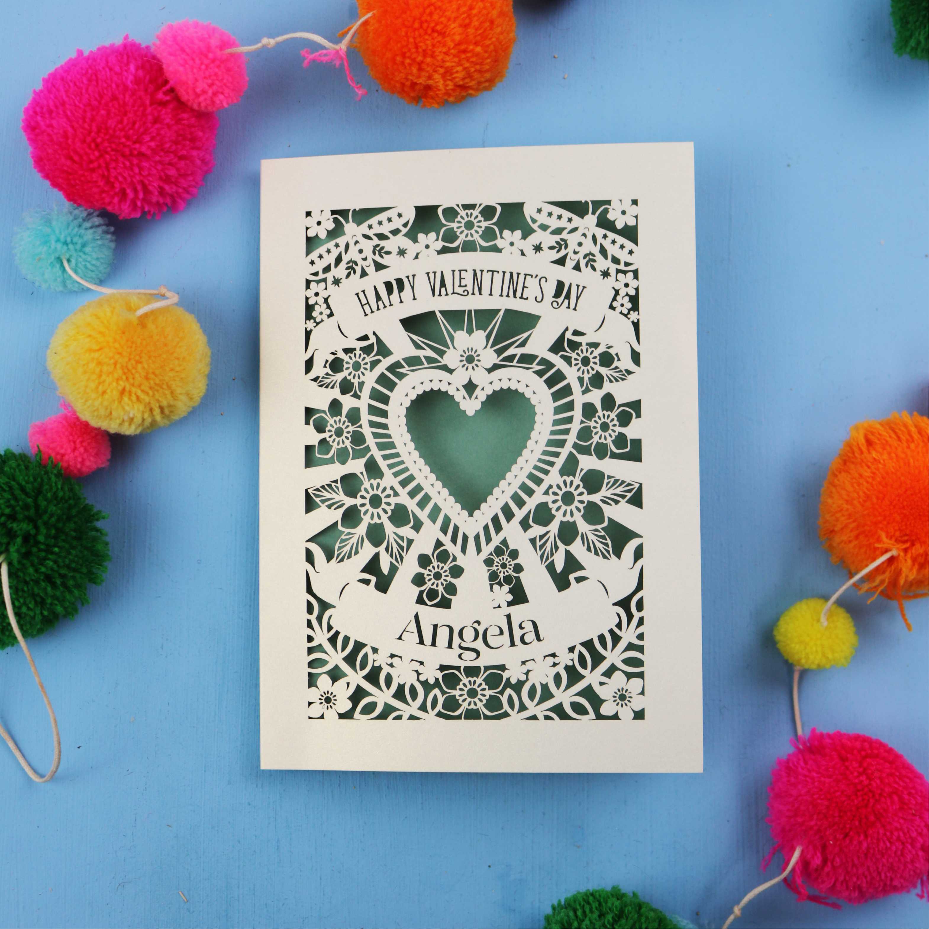 Luxury laser cut Valentine's Day card with decorative heart design on a blue background with colourful pom-poms.