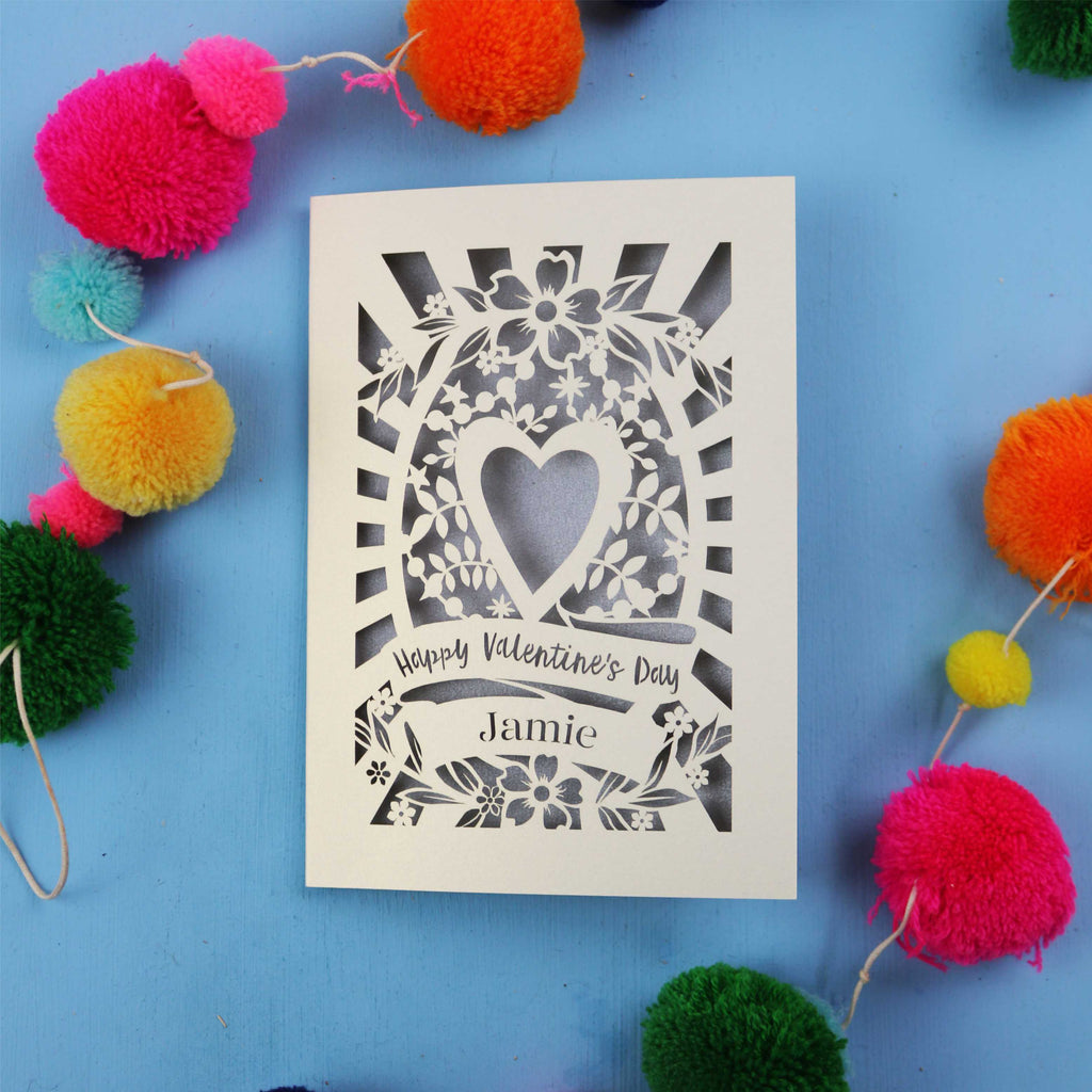 Decorative Valentine's card with floral heart design on a blue background with colourful pom-poms.