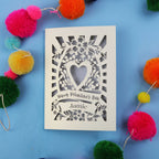Decorative Valentine's card with floral heart design on a blue background with colourful pom-poms.