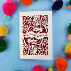 Laser cut Valentines Card for him, with decorative king of hearts cut-out design and text on a blue background with colourful pom-poms.