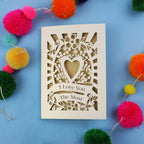 Laser cut Valentines Card with 'I Love You The Most' design on a blue background with colourful pom-poms.