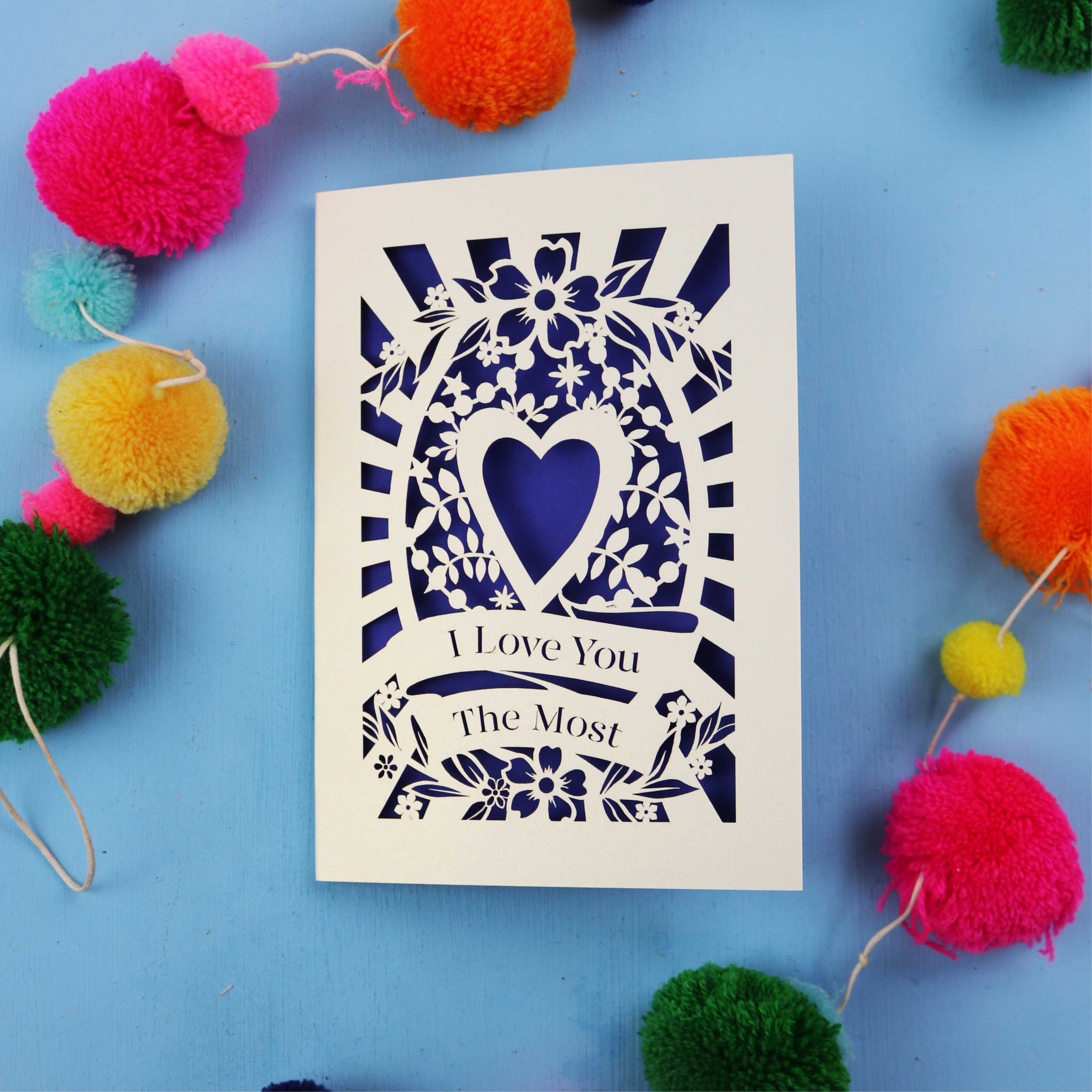 Valentines Card with 'I Love You The Most' design on a blue background with colourful pom-poms.