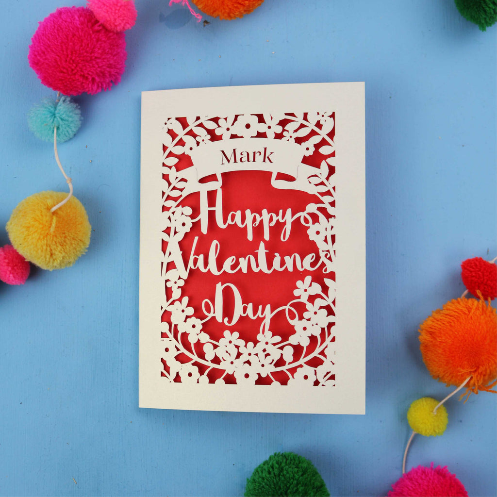 Personalised laser cut Valentine's Day card with decorative text on a blue background with colourful pom-poms.