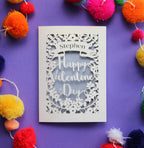 A card for Valentine's day, laser cut and personalised. Card has a name in a banner and the words "Happy Valentine's Day" surrounded by floral details