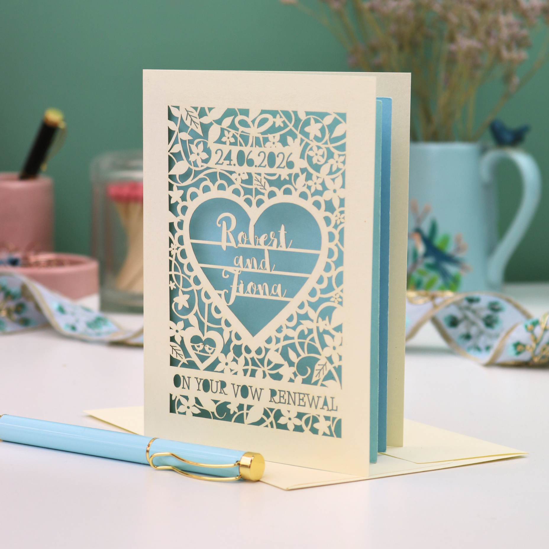 Laser-cut vow renewal card with decorative design and text on a table with stationery items.