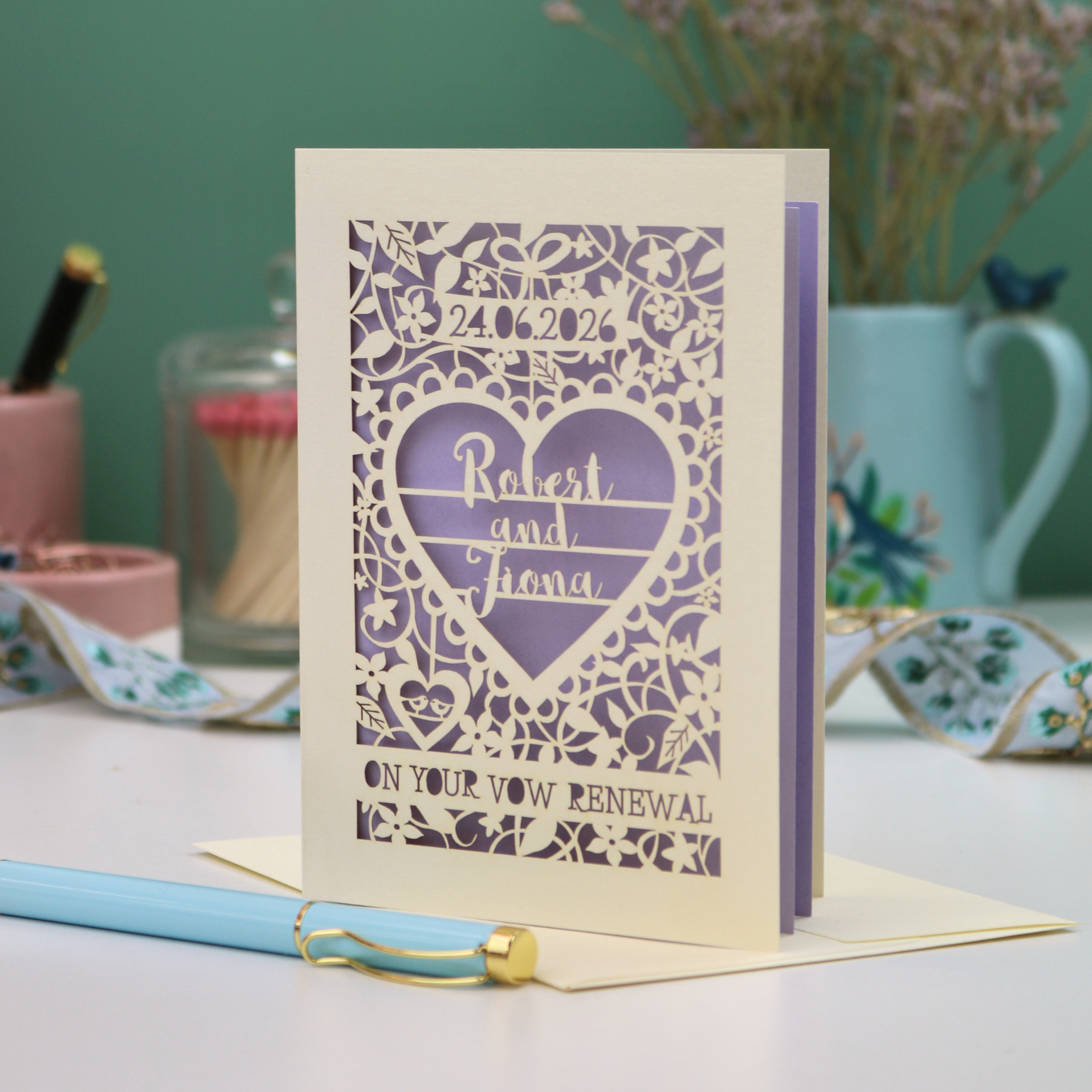 Laser-cut card with personalized text on a table with stationery items.