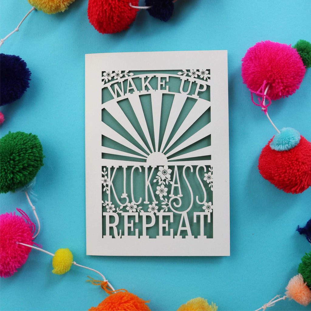A cut out motivational card that says "Wake up, Kick ass, repeat"