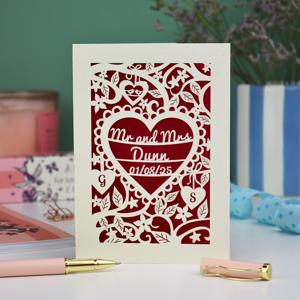 Personalised cut out wedding anniversary card with decorative heart design and 'Mr and Mrs Dunn' text, placed on a surface with stationery items.