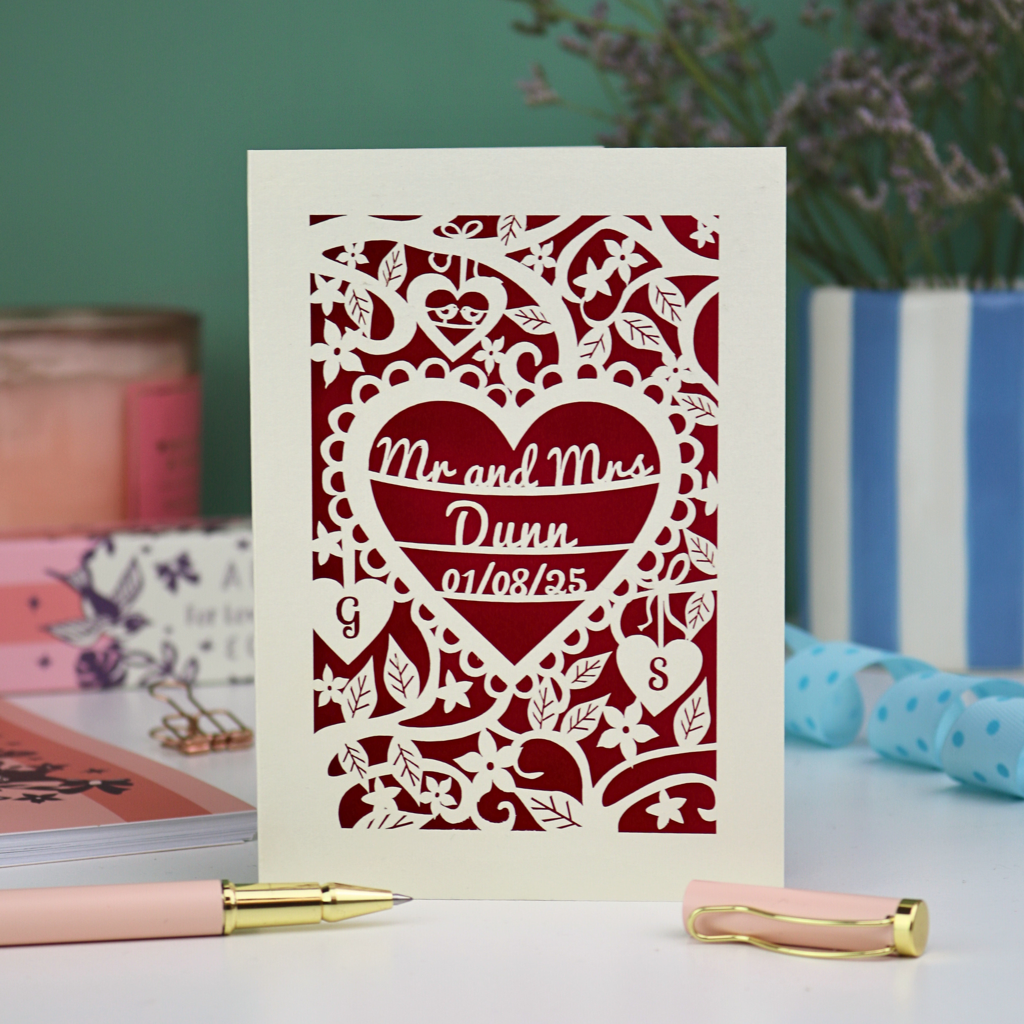 Personalised cut out wedding anniversary card with decorative heart design and 'Mr and Mrs Dunn' text, placed on a surface with stationery items.