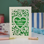 Personalised anniversary card with decorative heart design and 'Mr and Mrs Dunn' text, placed on a surface with stationery items.