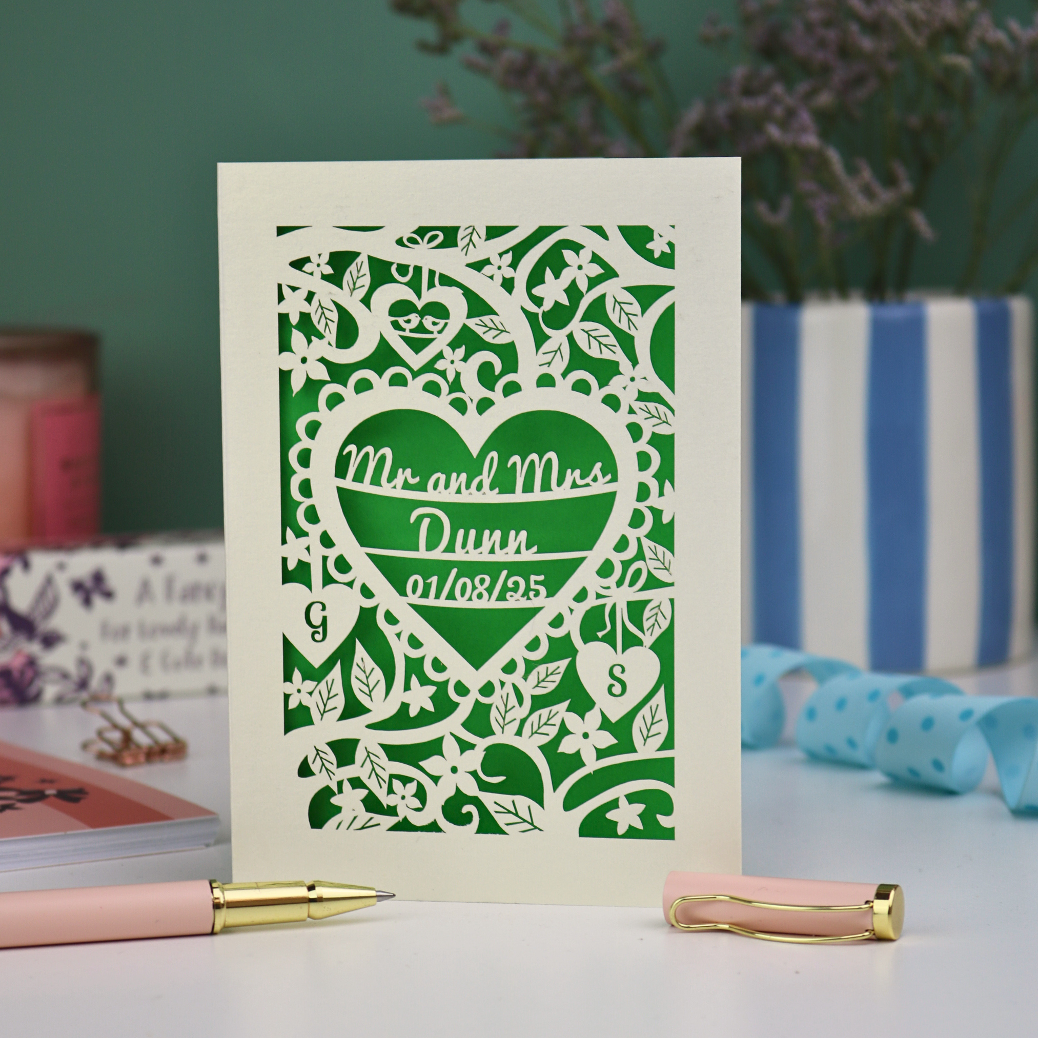 Personalised anniversary card with decorative heart design and 'Mr and Mrs Dunn' text, placed on a surface with stationery items.