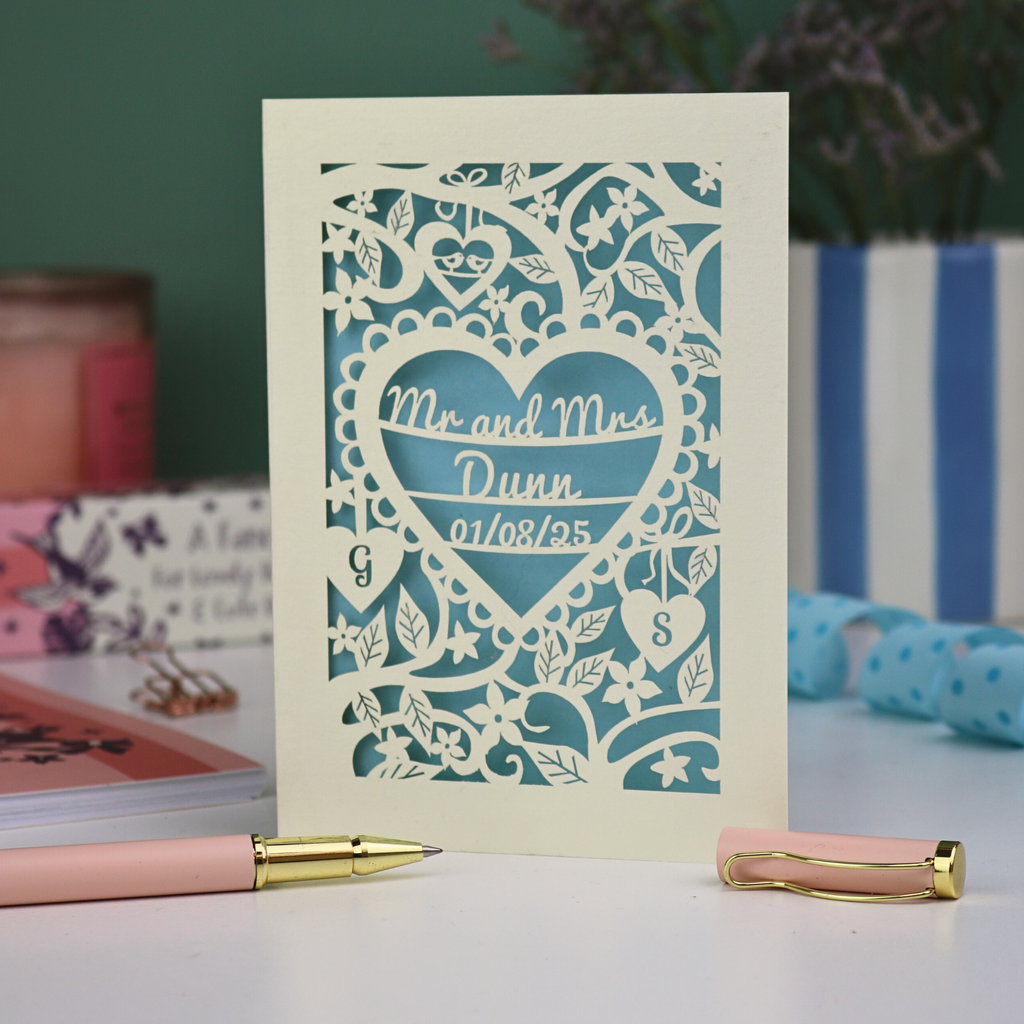Personalised wedding anniversary card with decorative heart design and 'Mr and Mrs Dunn' text, placed on a surface with stationery items.