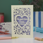 Personalised laser cut wedding anniversary card with decorative heart design and 'Mr and Mrs Dunn' text, placed on a surface with stationery items.