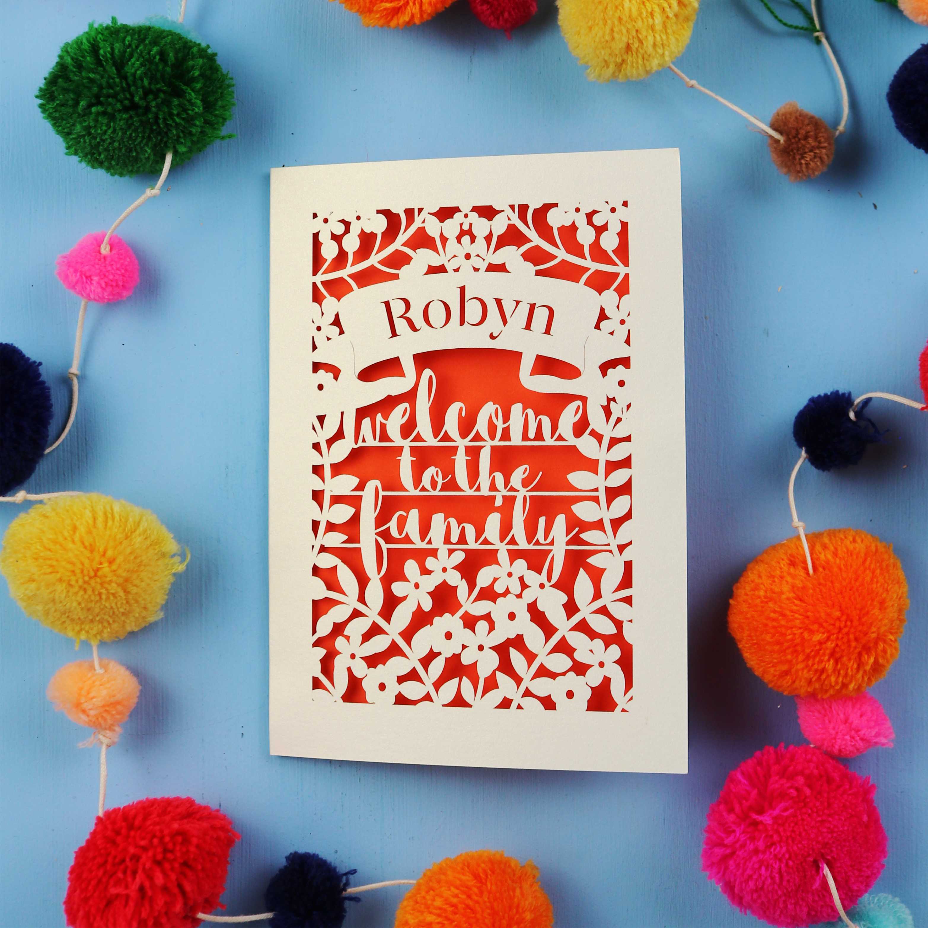 Wedding card with 'Robyn Welcome to the Family' text on a blue background with colourful pom-poms.