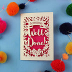 Decorative card with 'Well Done' text on a blue background with colouful pom-poms.