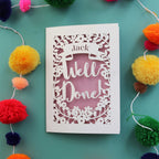 A personalised celebration card that says "Well Done" and has the recipient's name in a banner