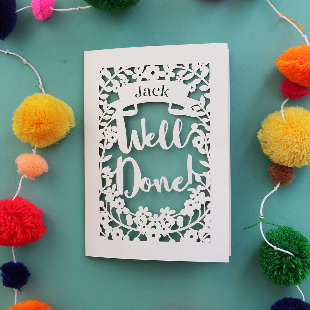 A personalised laser cut achievement card that says "Well Done" and has the recipient's name in a banner