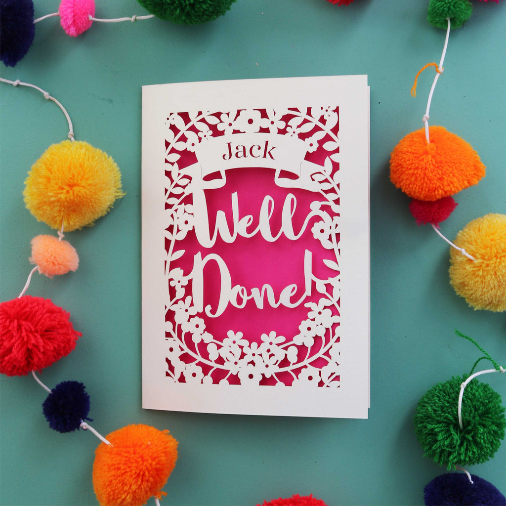A personalised cut out celebration card that says "Well Done" and has the recipient's name in a banner