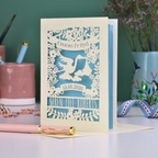 Personalised cut out Welsh New Baby card with stork design and text: "Croeso I'r Byd", personalised with the date of birth and baby's name, on a blurred background