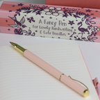 Pink pen with gold accents on a white surface, next to its packaging box.