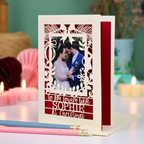A personalized laser-cut Christmas greeting card with a photo of a couple, displayed on a table with candles and pencils in a cosy setting. Card says 'To my lovely wife Sophie at Christmas'