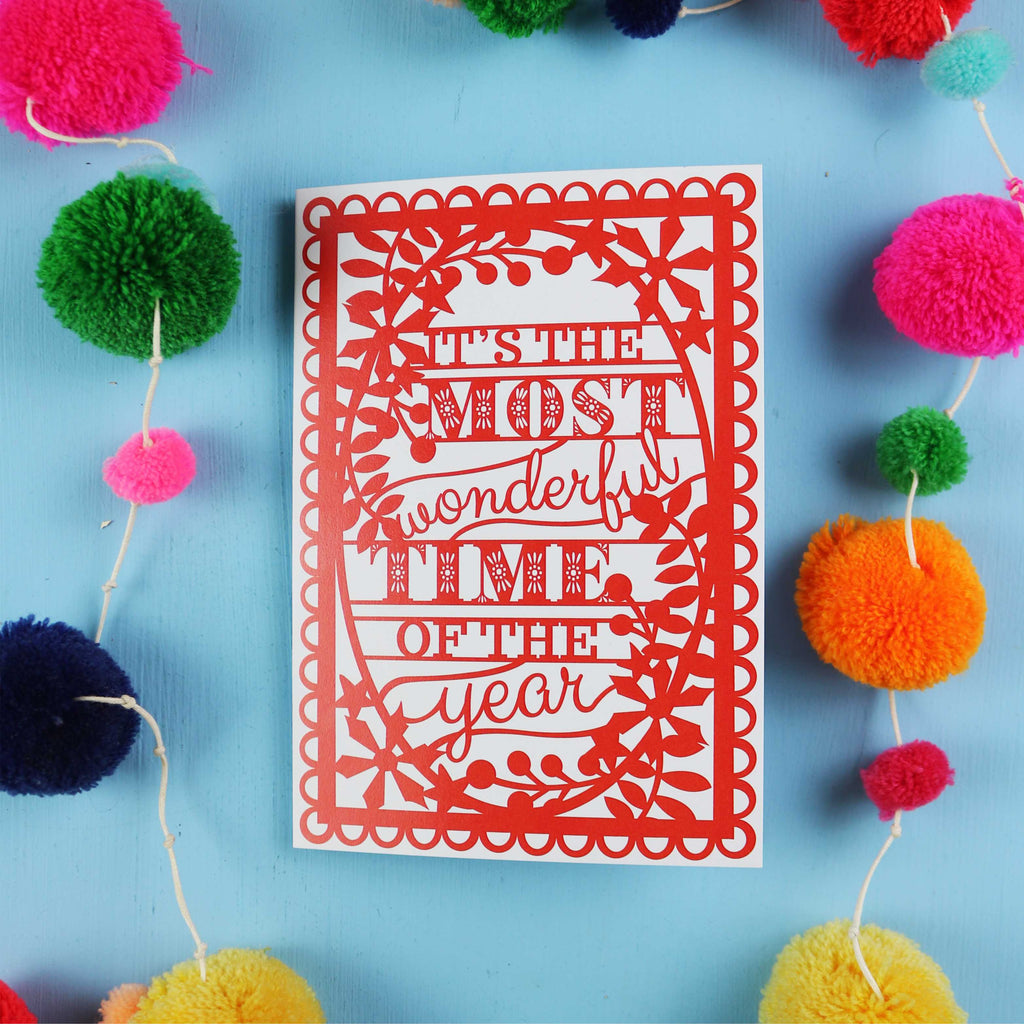 Decorative card with 'It's the most wonderful time of the year' text on a blue background with colourful pom-poms.