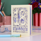 Decorative keepsake 18th birthday card with '18' and personalised with the name 'Willow', featuring floral designs and woodland creatures. Card stands on a desk with stationery items.