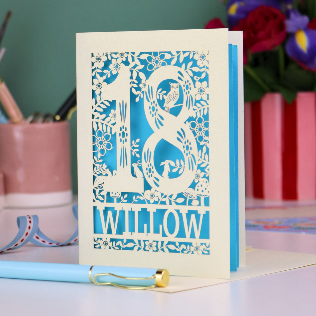Decorative laser cut  special 18th birthday card with '18' and personalised with the name 'Willow', featuring floral designs and woodland creatures. Card stands on a desk with stationery items.