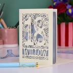 Decorative laser cut 18th birthday card with '18' and personalised with the name 'Willow', featuring floral designs and woodland creatures. Card stands on a desk with stationery items.