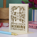A laser cut 1st birthday card with decorative 1 and woodland design including owl, bunnies, squirrel and hedgehog, personalised with a name.