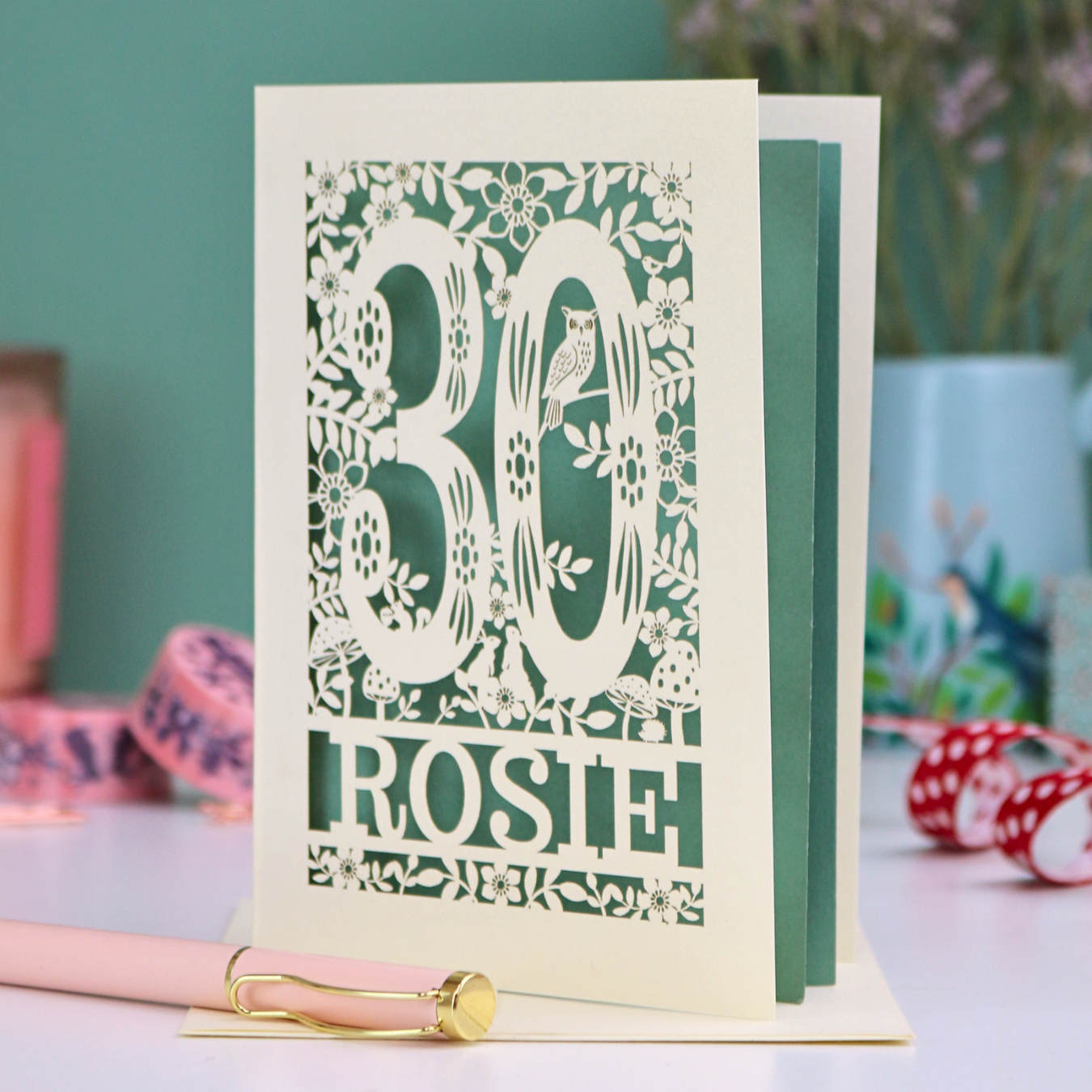 Laser-cut woodland 30th birthday card with decorative text and illustrations on a table with stationery items.