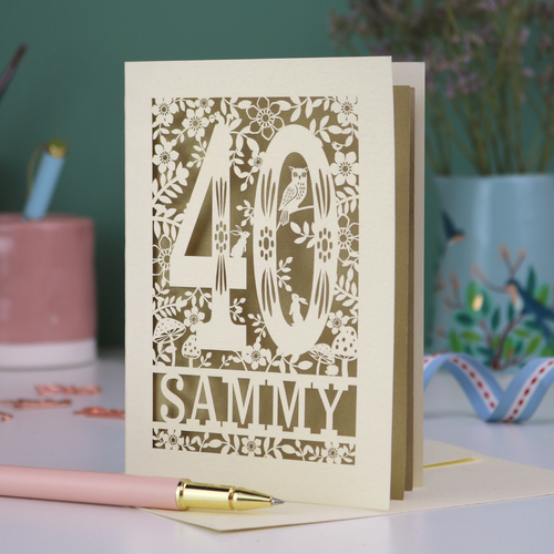 A laser cut 40th birthday card with woodland design, decorative number '40 and personalised with a name, 'Sammy', on a white desk with pen and stationery items