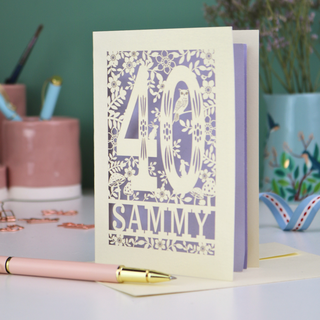 A laser cut 40th birthday card with woodland design, decorative number '40 and personalised with a name, 'Sammy', on a white desk with pen and stationery items