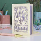A laser cut 40th birthday card with woodland design, decorative number '40 and personalised with a name, 'Sammy', on a white desk with pen and stationery items